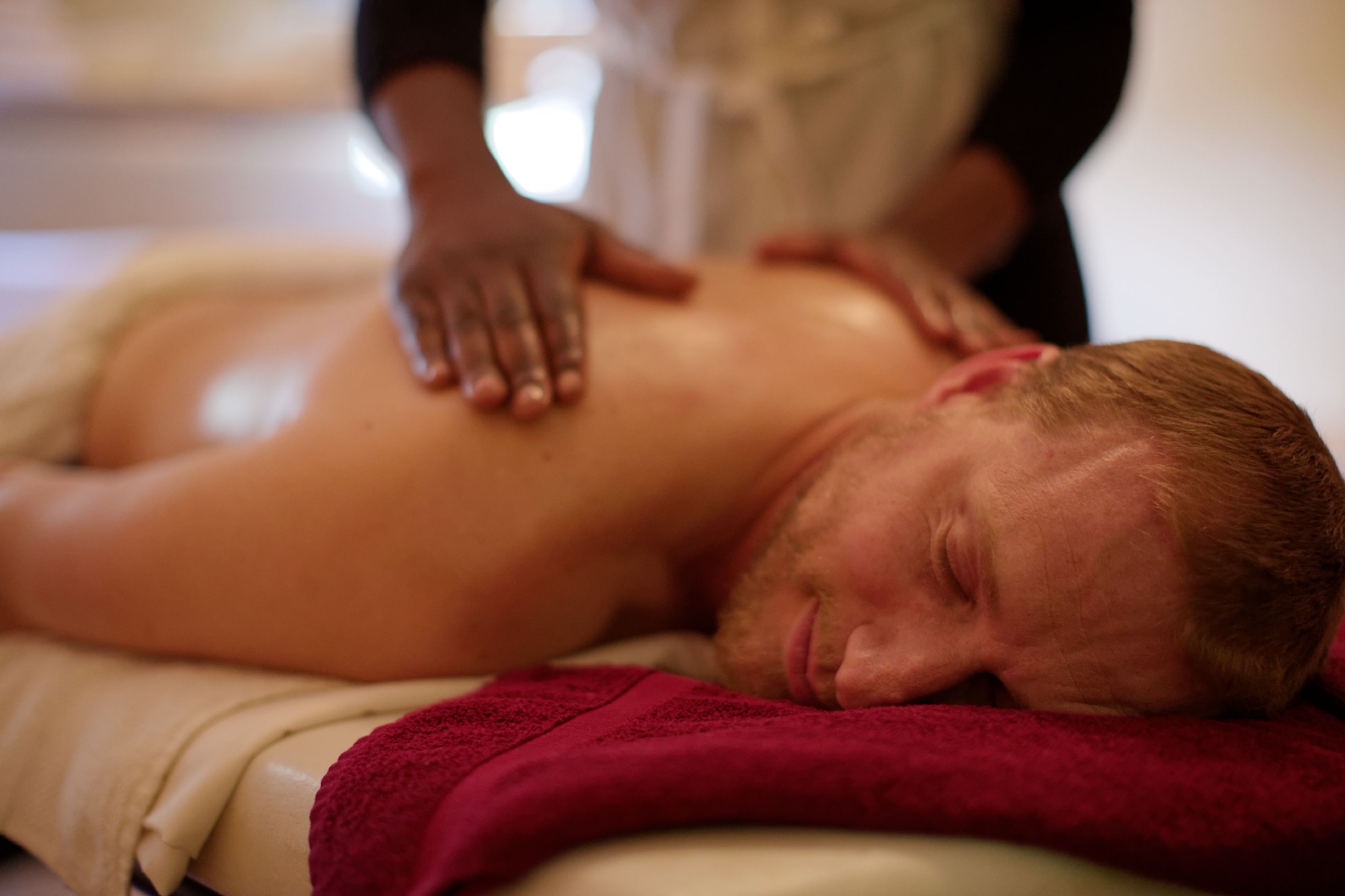A person receiving a back massage in a room with a red towel and a white bedspread.