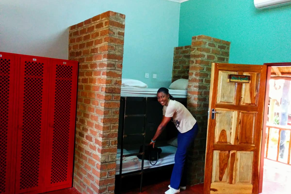 A room with a brick wall, a bunk bed, a red wardrobe, and a wooden door.