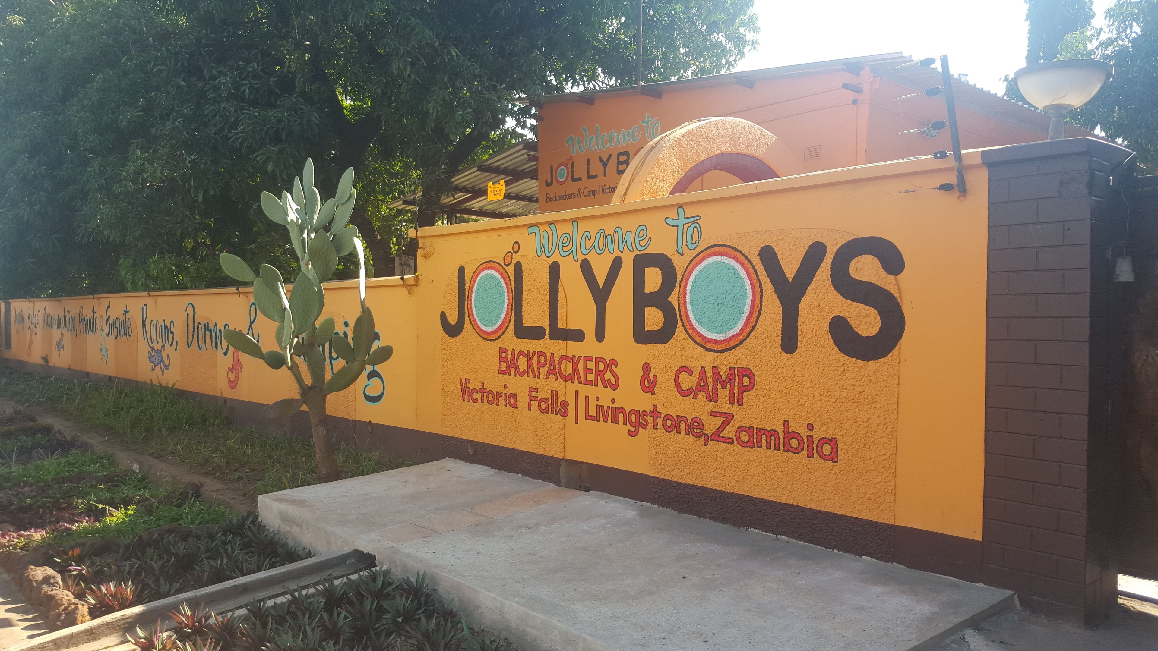 Pared con un letrero que da la bienvenida a visitantes a Jollyboys Backpackers & Camp en Victoria Falls, Zambia.