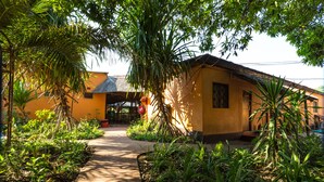 A building with a thatched roof, surrounded by lush greenery and a concrete pathway. - Jollyboys Backpackers (Livingstone)