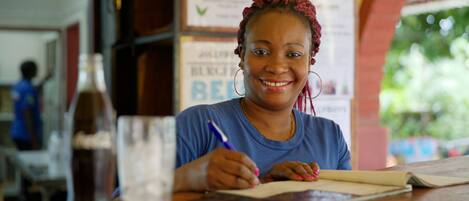 A person sitting at a wooden table with a notebook and pen, a bottle of Coca-Cola, and a glass of water.