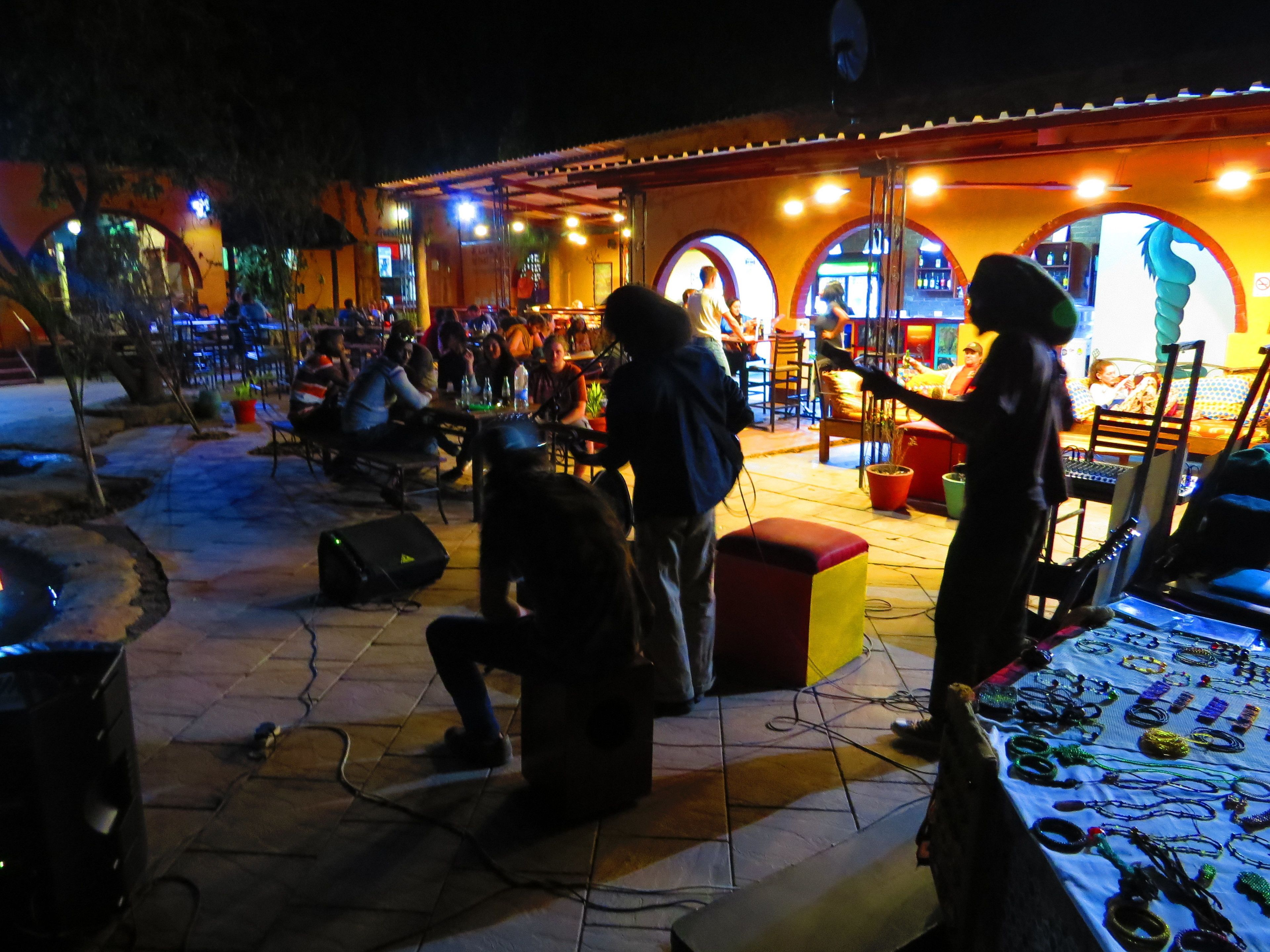 Area esterna con posti a sedere, tavoli e sedie, un palco con un artista e uno stand che vende gioielli.