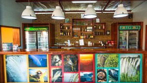 A bar with a brick wall, shelves with bottles, and a JollyBoys refrigerator. - Jollyboys Backpackers (Livingstone)