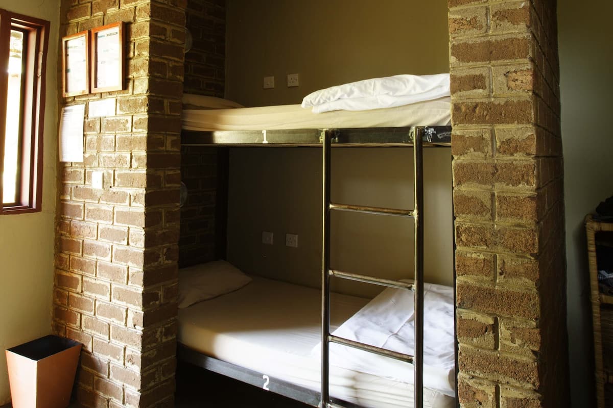 A bunk bed room with brick walls, a window, and a trash bin.