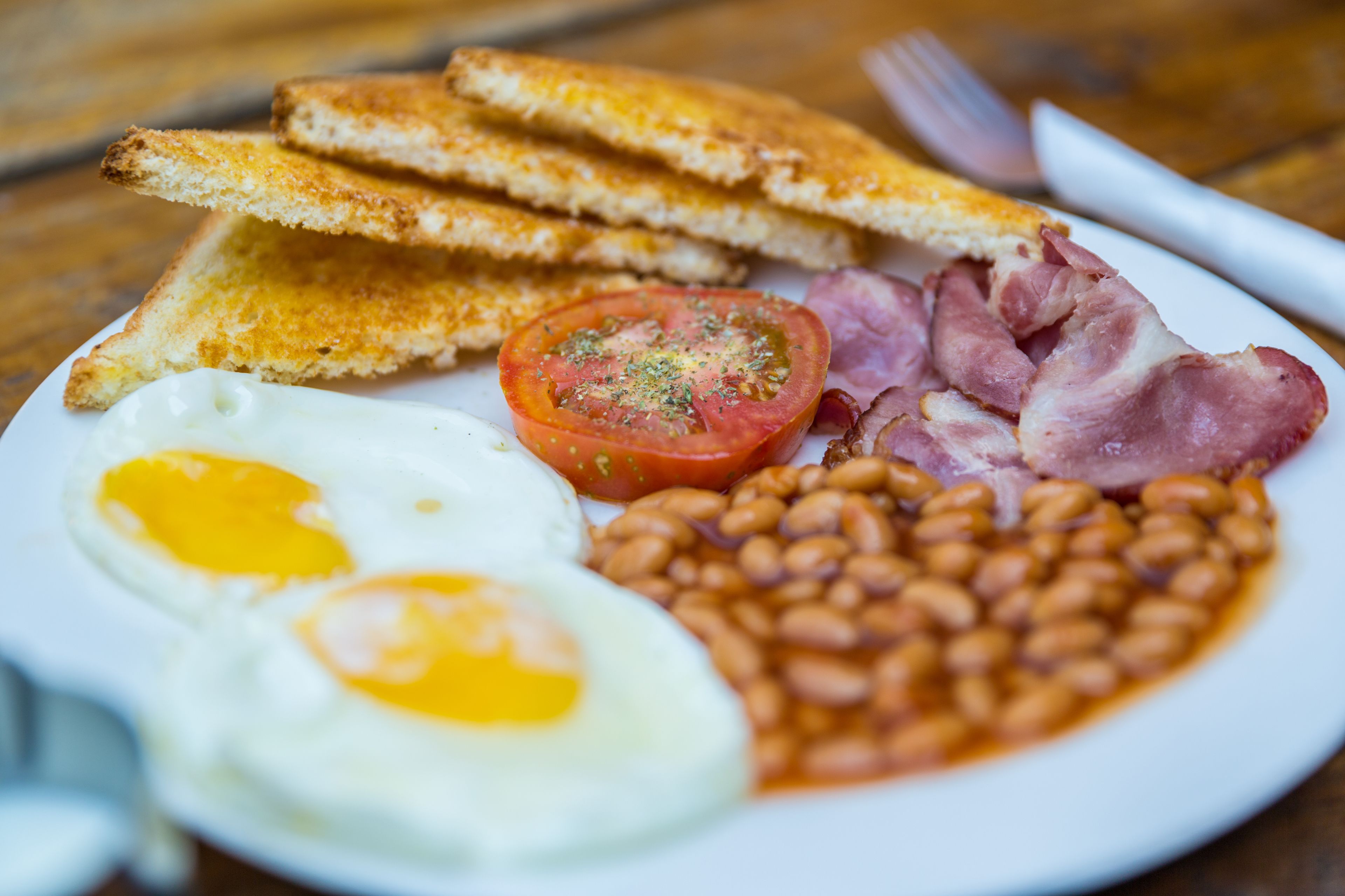 A plate of breakfast food including toast, eggs, bacon, beans, and a tomato.
