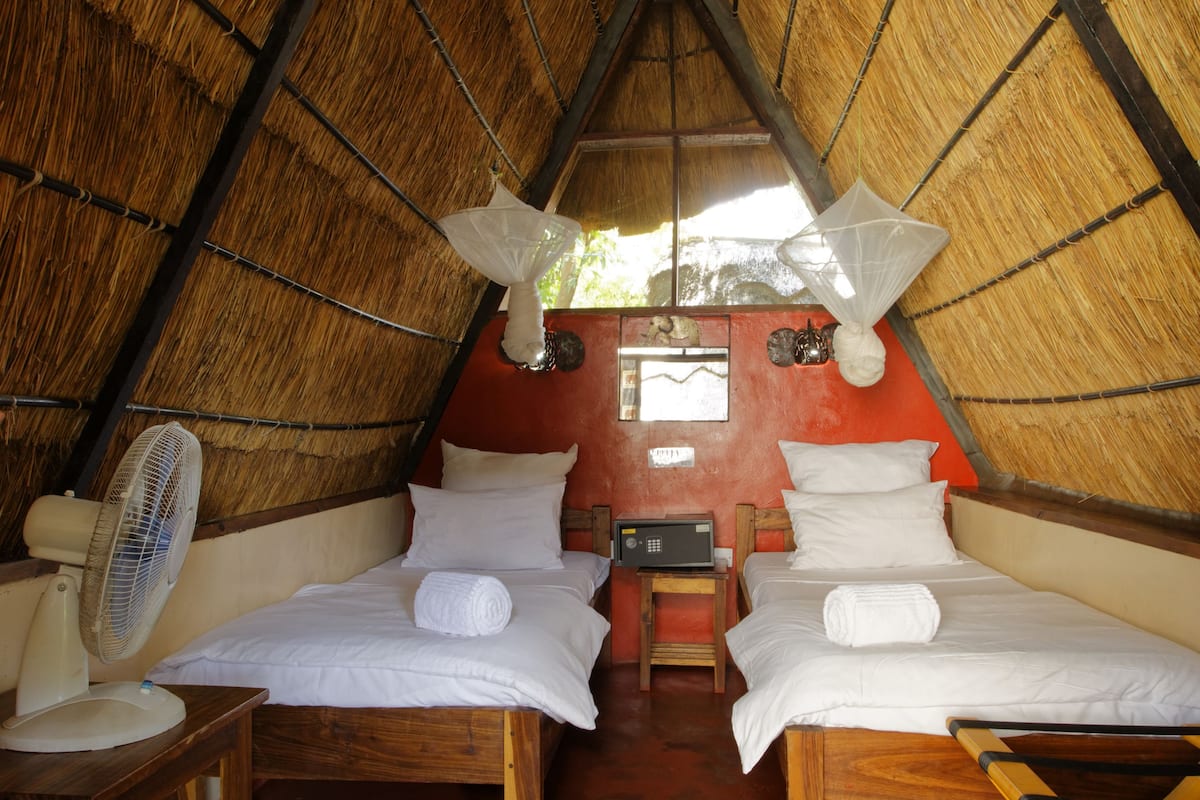 A room with two beds, a fan, a wooden table, and a window.