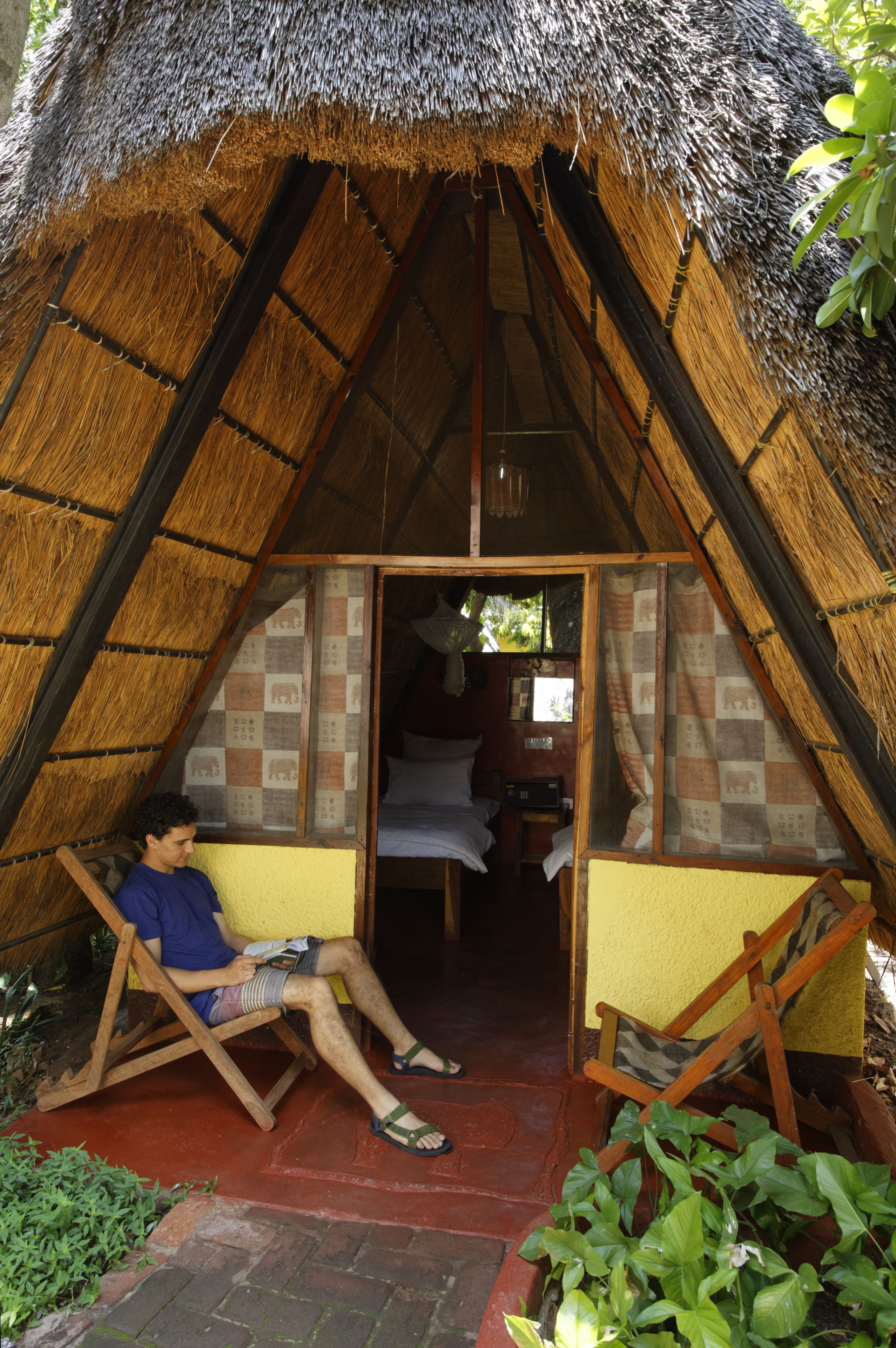 A thatched-roof structure with a sloped roof, a small entryway, and a single bed visible inside.