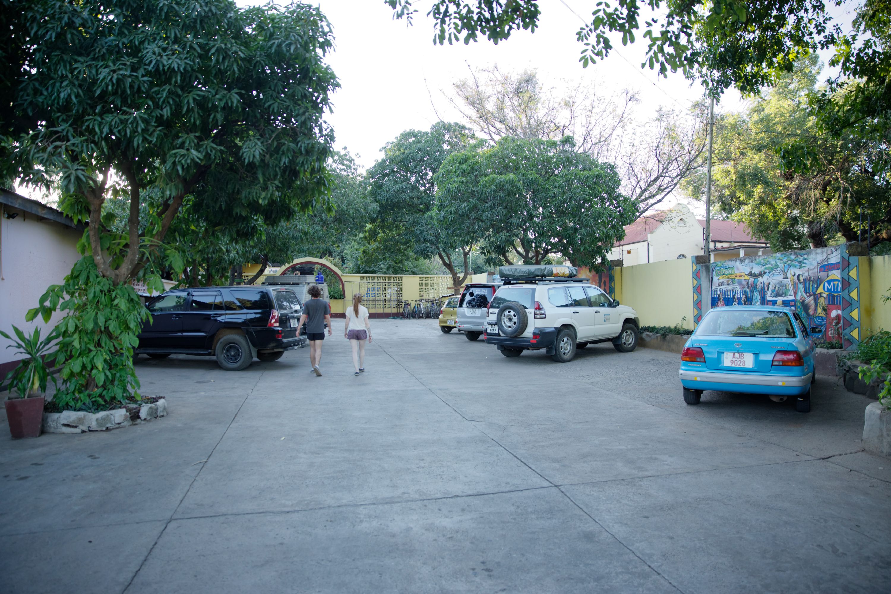 A parking lot with several cars and a few people walking.