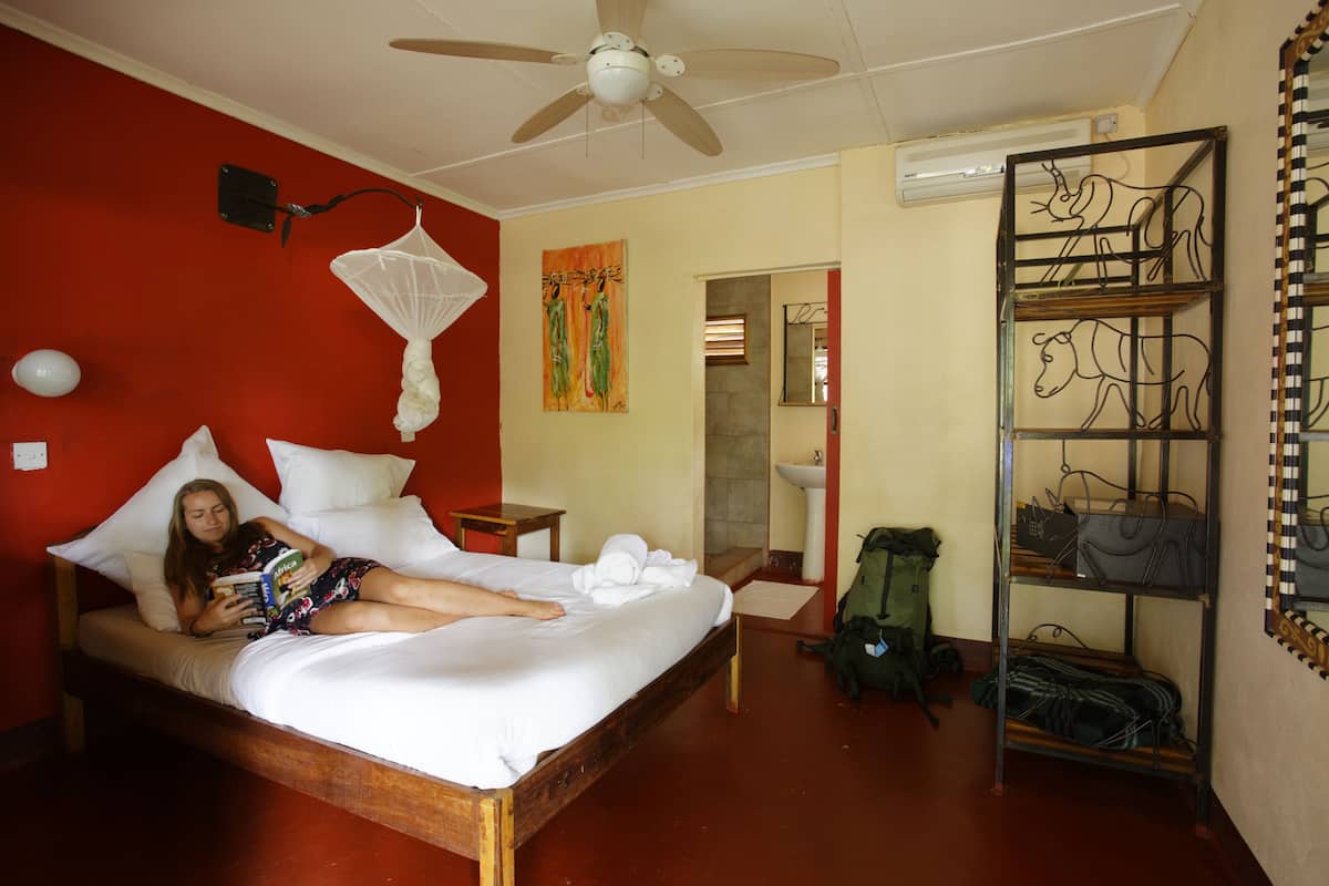 A room with a bed, a ceiling fan, a bedside table, a green backpack, and a metal rack with bags.