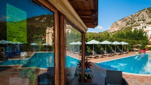 Zona junto a la piscina con sillones reclinables y sombrillas, con vistas a una montaña y un cartel con información de contacto.