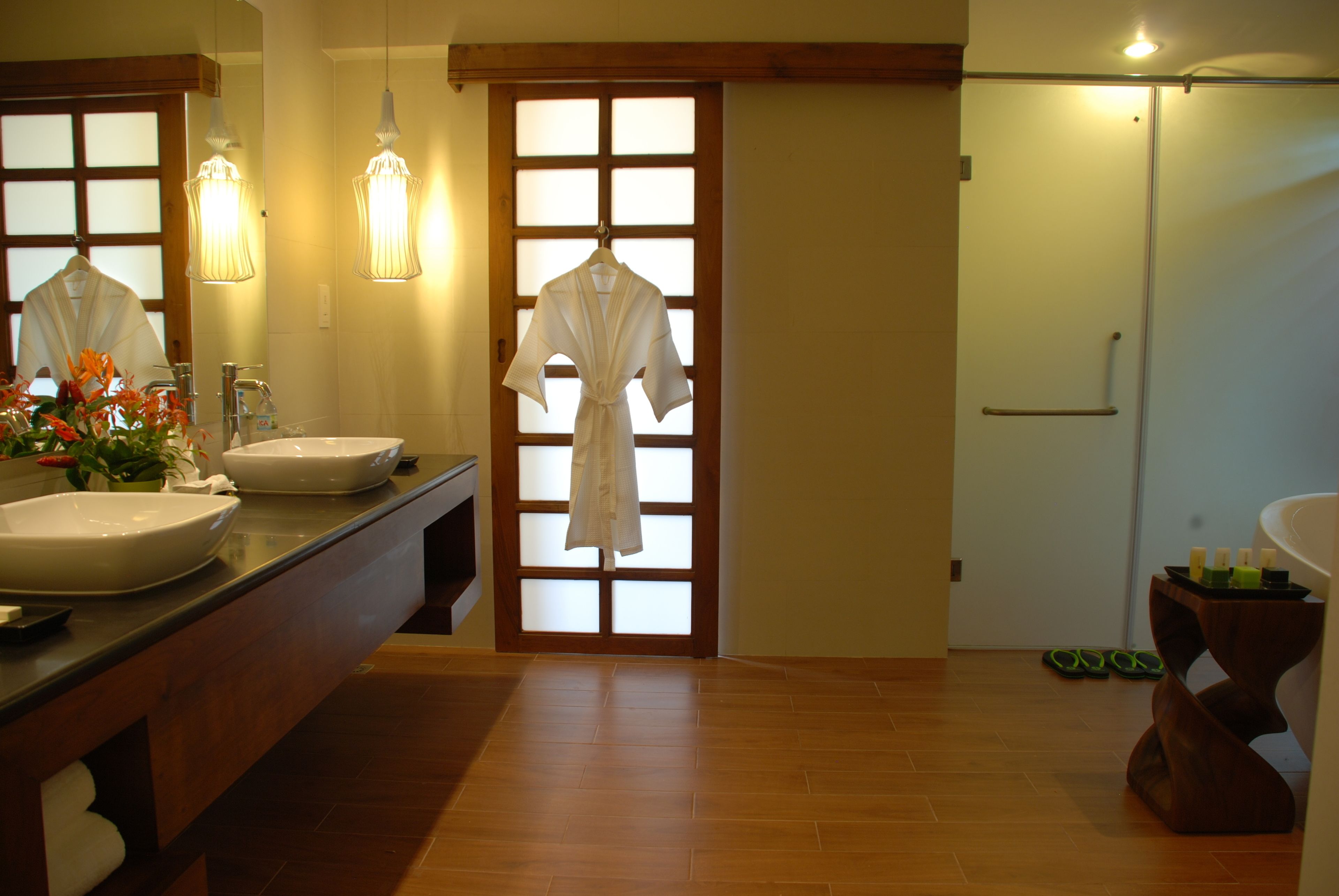 A bathroom with two sinks, a robe hanging by the door, and a shower area.