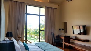 Habitación de hotel con un ventanal grande, una cama, un escritorio con silla, un televisor y una lámpara.