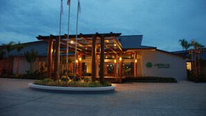 Entrada de un hotel con un área exterior cubierta, banderas y un letrero que indica que es el Nirvana Hotel & Resort.