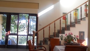 A hotel lobby with a staircase, wooden chairs, a table with a white tablecloth, and a potted plant. - Suoi Nuoc Resort (Mui Ne)
