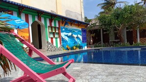 A pool area with a mural of dolphins, a pink chair, and a building with colorful stripes and a blue awning. - Suoi Nuoc Resort (Mui Ne)