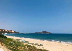 A beach with clear skies, a sandy shore, and a distant hill.
