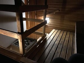 A wooden cabin interior with a bunk bed, a small storage box, and a light source on the wall.