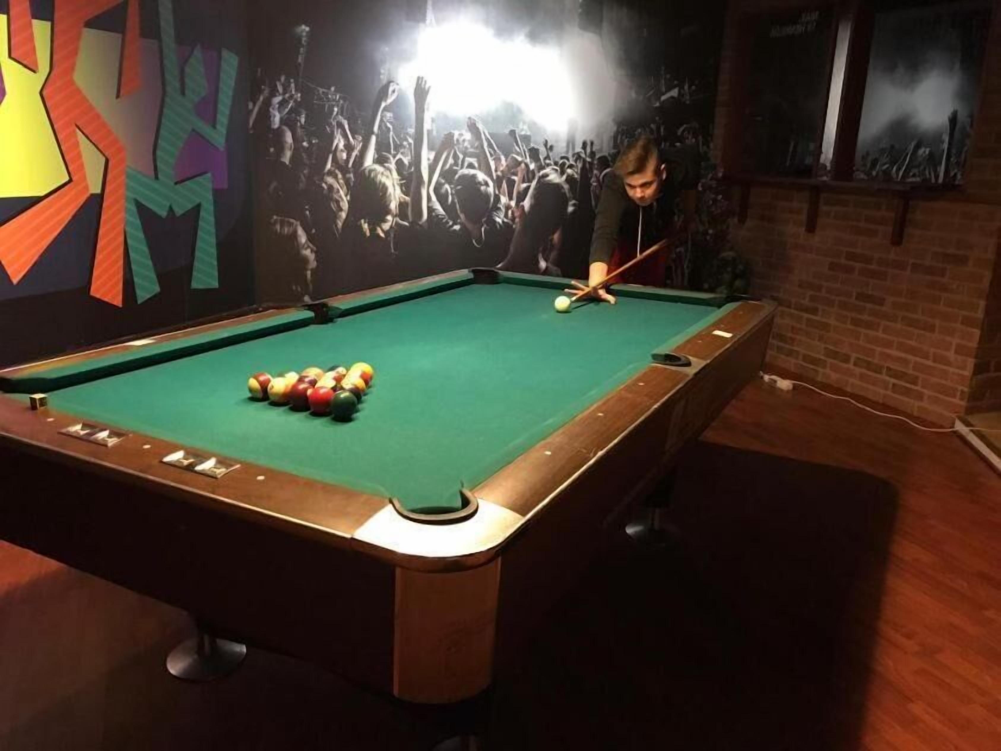 A pool table with balls in the center, surrounded by a brick wall and a mural.