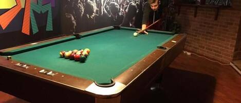 A pool table with balls in the center, surrounded by a brick wall and a mural.