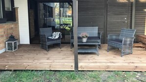 Une terrasse extérieure avec une plateforme en bois, deux fauteuils en osier, une table et un pot de fleurs.