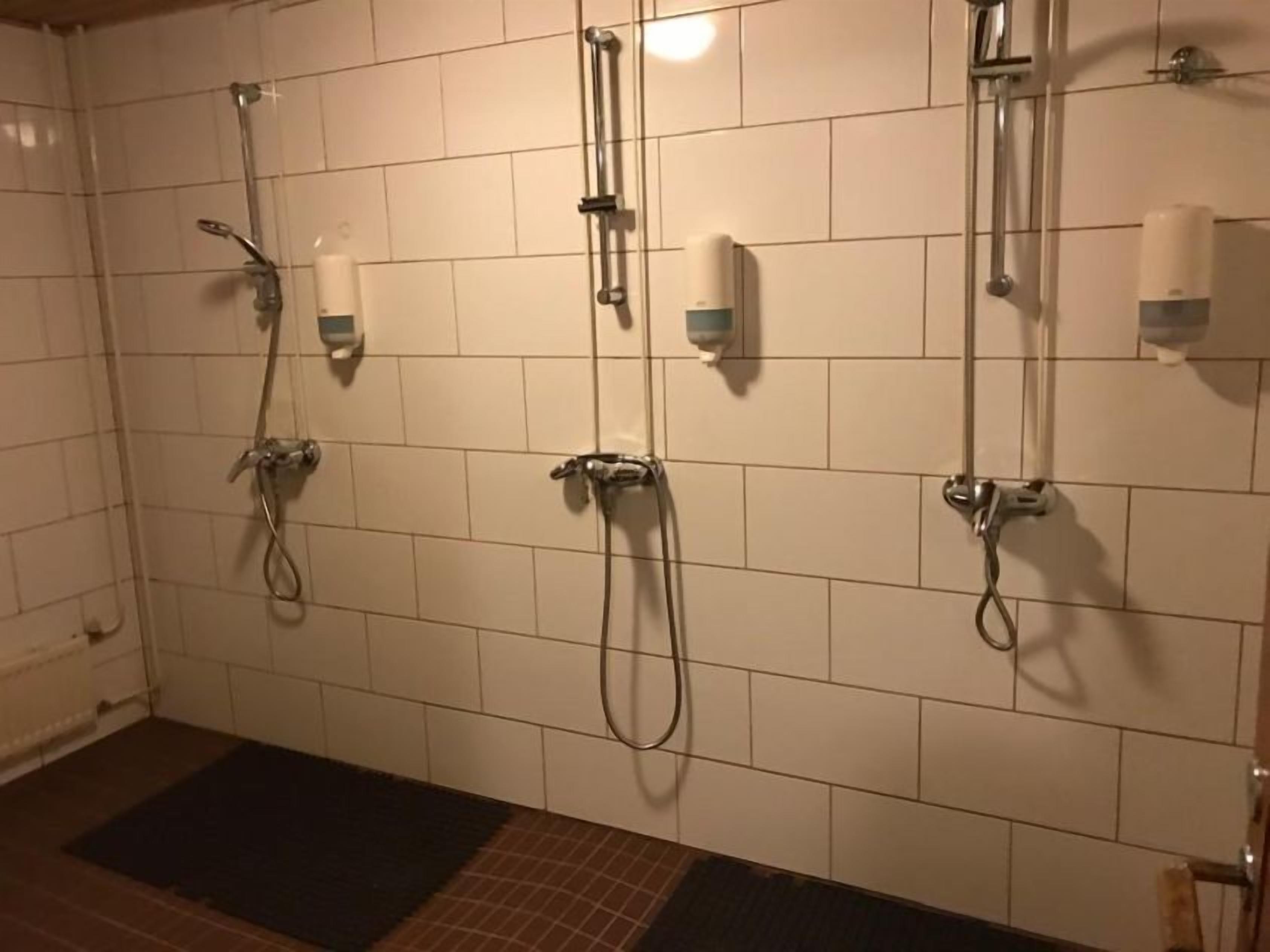 Zona de ducha con múltiples cabezales de ducha y secadores de manos en la pared.