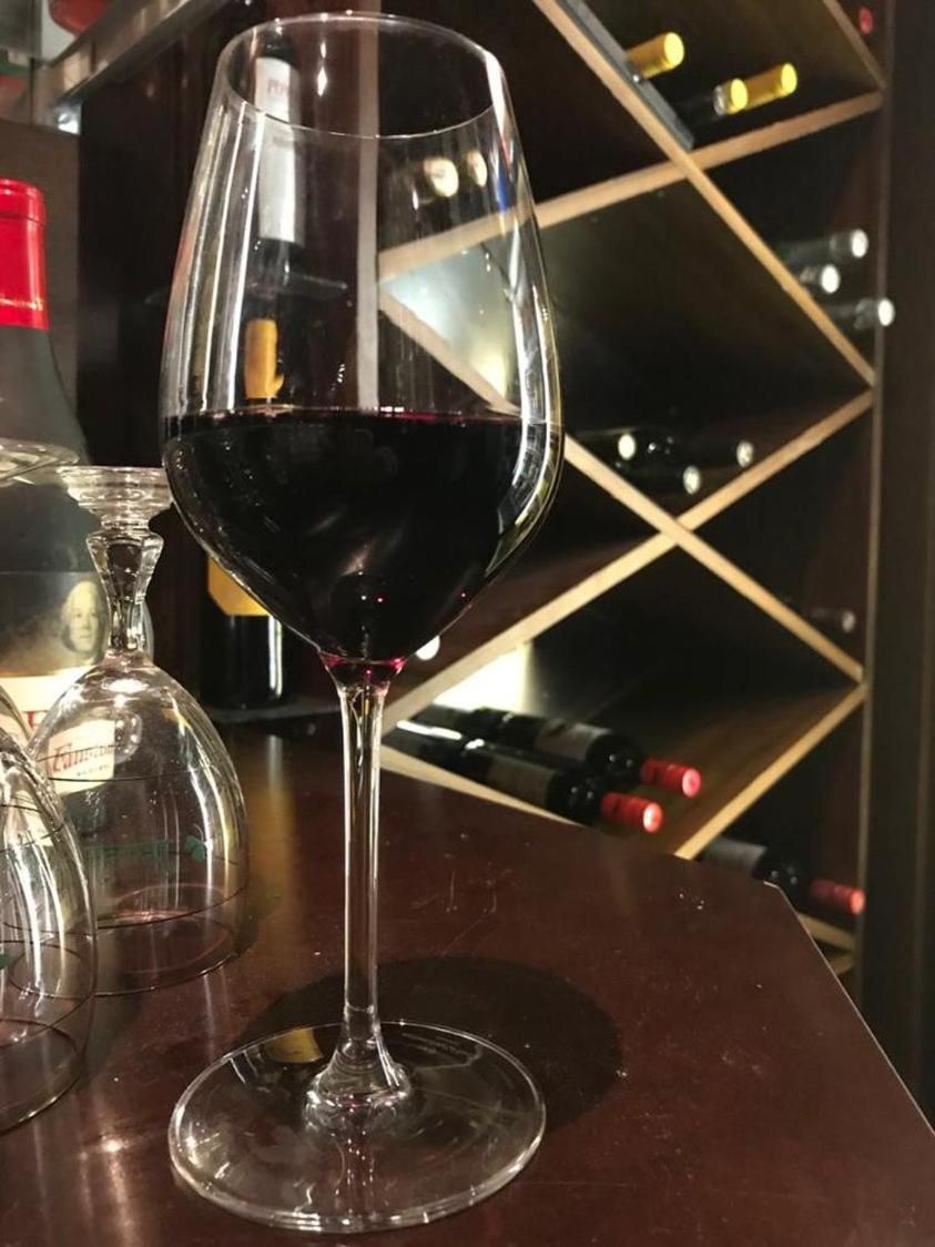 A wine glass filled with red wine on a bar counter with a wine rack in the background.