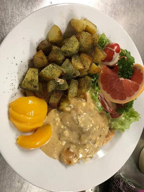 A plate with roasted potatoes, a slice of grapefruit, a creamy sauce, and a salad with lettuce and radish.