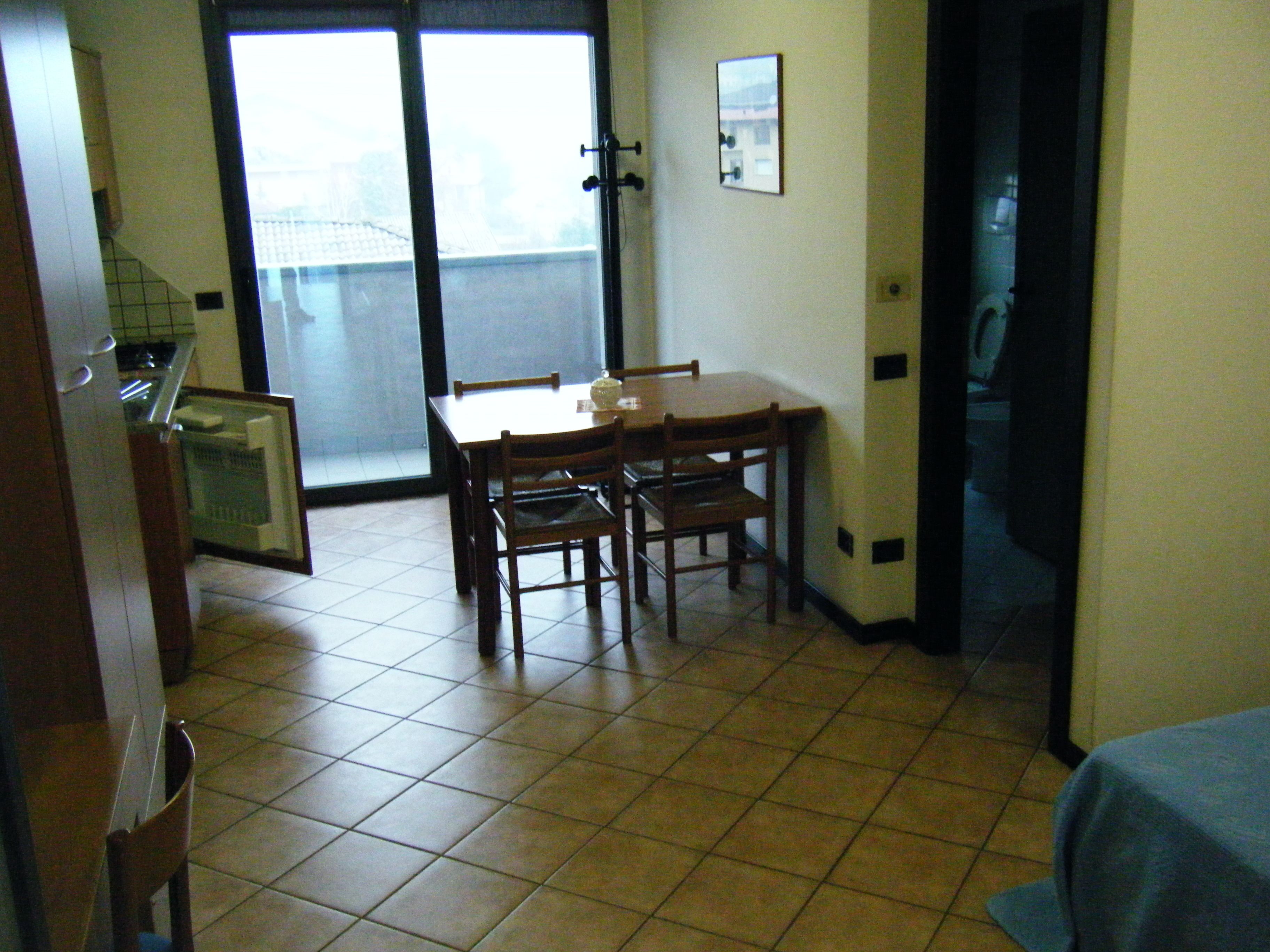 Un'angolatura sala da pranzo con tavolo e sedie, un frigorifero e una finestra vista esterna.