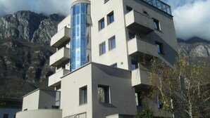 A modern building with multiple floors, balconies, and a cylindrical glass tower. - Residence Vezzoli (Darfo Boario Terme)