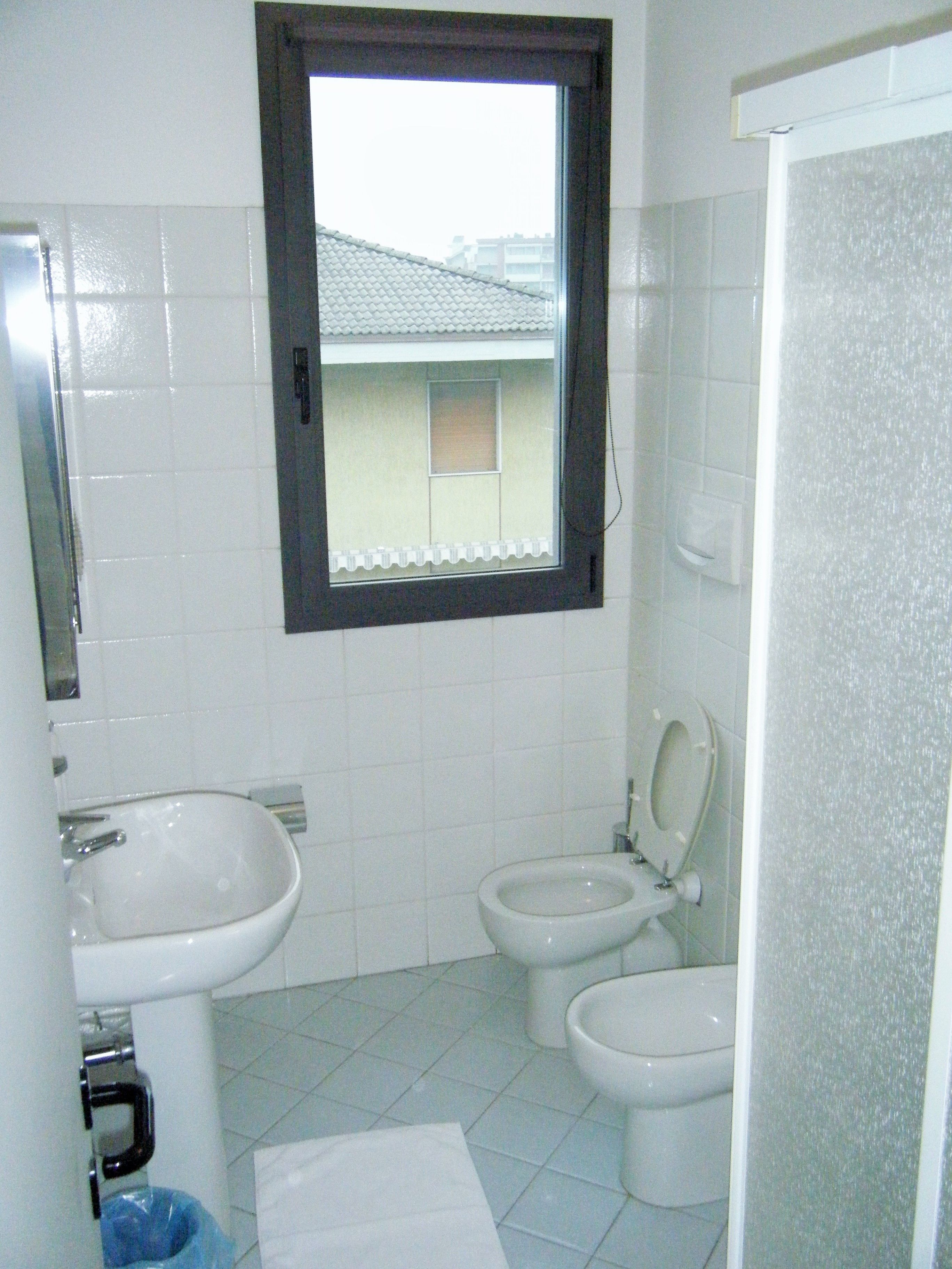 Een badkamer met een wastafel, twee toiletten en een raam.