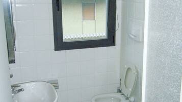 Een badkamer met een wastafel, twee toiletten en een raam.
