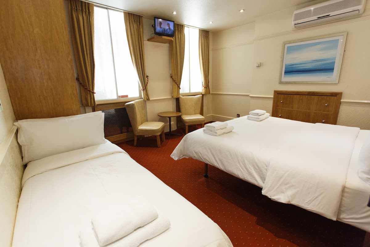 A hotel room with two beds, a TV, a small table, and a chair.