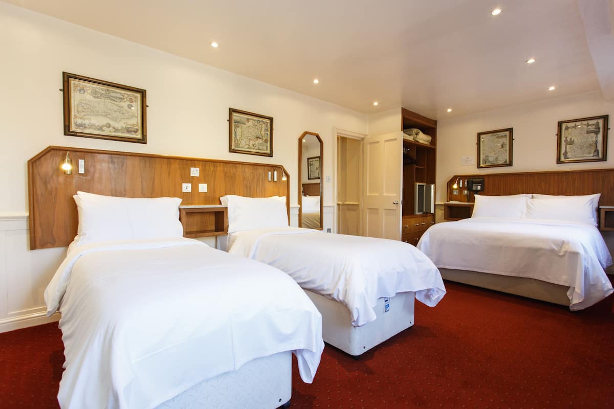 A hotel room with three single beds, wooden headboards, white bedding, and a red carpet.
