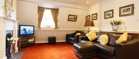 A living room with a red carpet, black leather sofa, a television, and framed pictures on the wall.