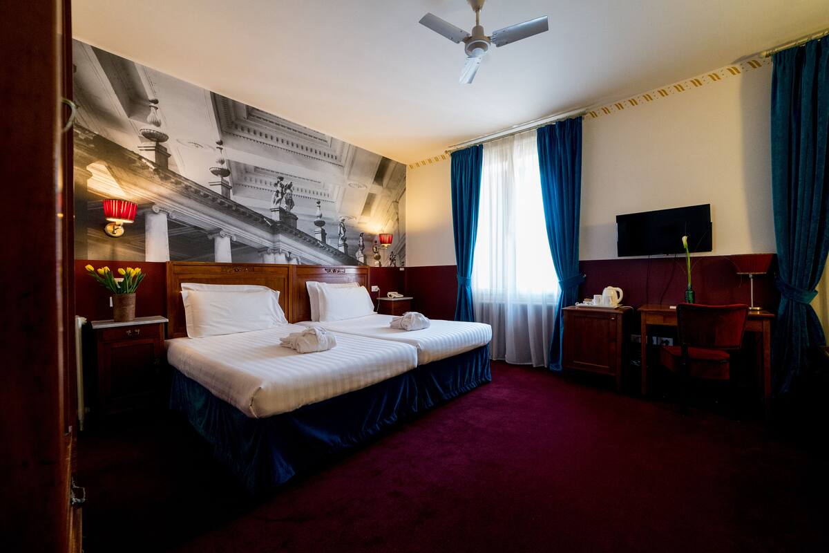 Een hotelkamer met een groot bed, een bureau, een stoel, een televisie en een plafondventilator.