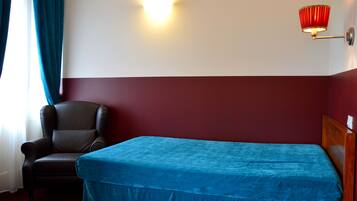 Una camera d'albergo con un letto, una sedia, una lampada a parete e una finestra con tende.