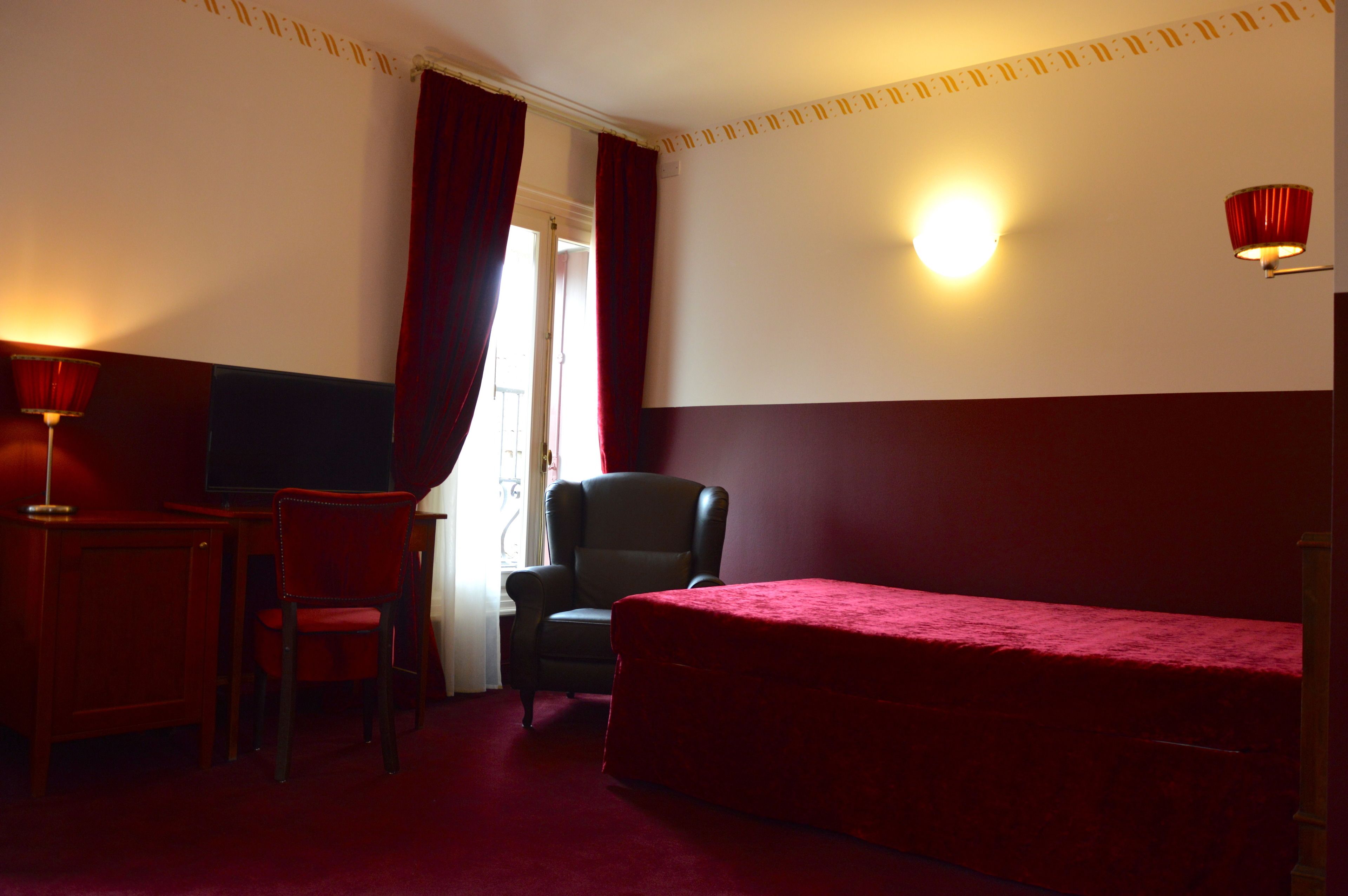 A hotel room with a bed, a desk with a chair, a television, and a wall-mounted light fixture.