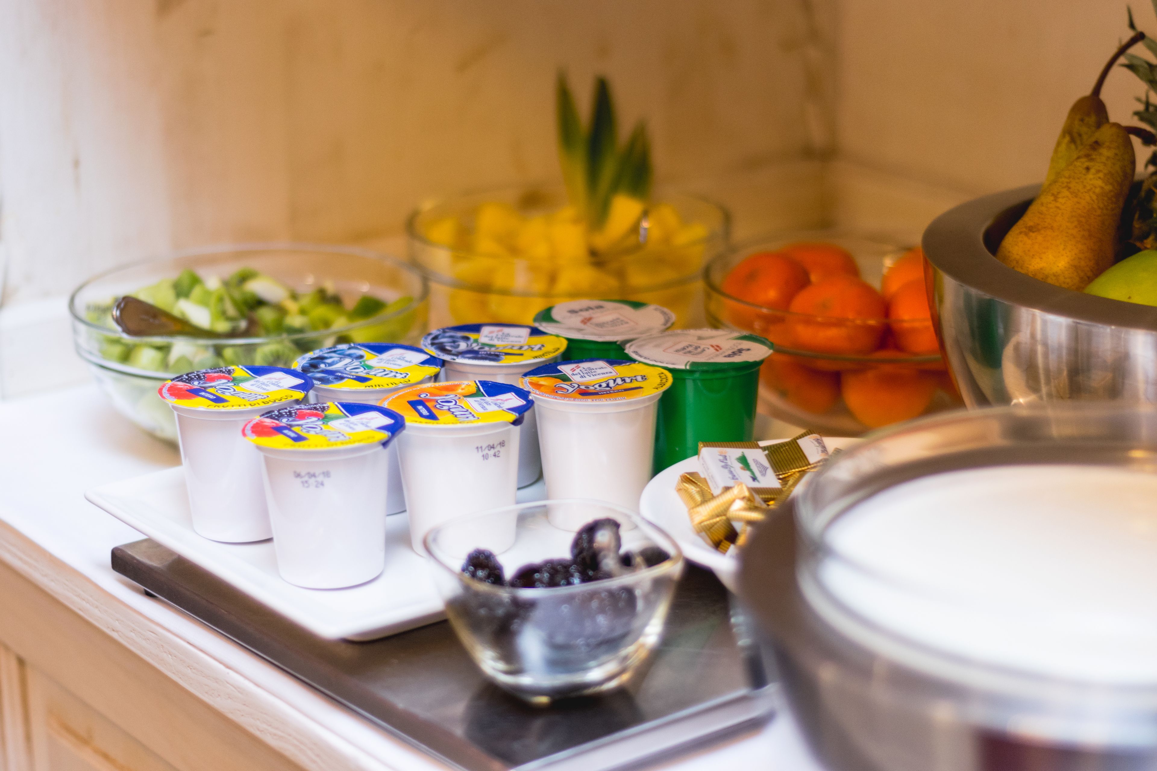 A kitchen counter with various food items and containers, including a bowl of fruit, a bowl of berries, and several cups with lids.