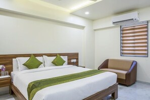 Une chambre d’hôtel avec un lit, une table de chevet, un canapé marron et une fenêtre avec des stores.