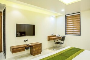 Une chambre moderne équipée d’un téléviseur à écran plat, d’un bureau en bois, d’une chaise et d’un lit agrémenté d’un couvre-lit vert.