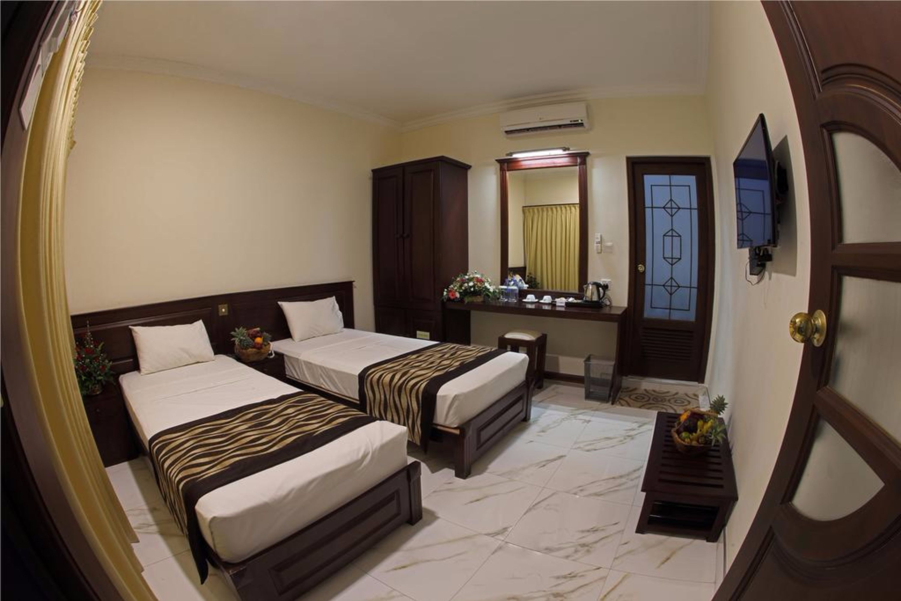 A hotel room with two beds, a desk, a mirror, an air conditioning unit, and a television.