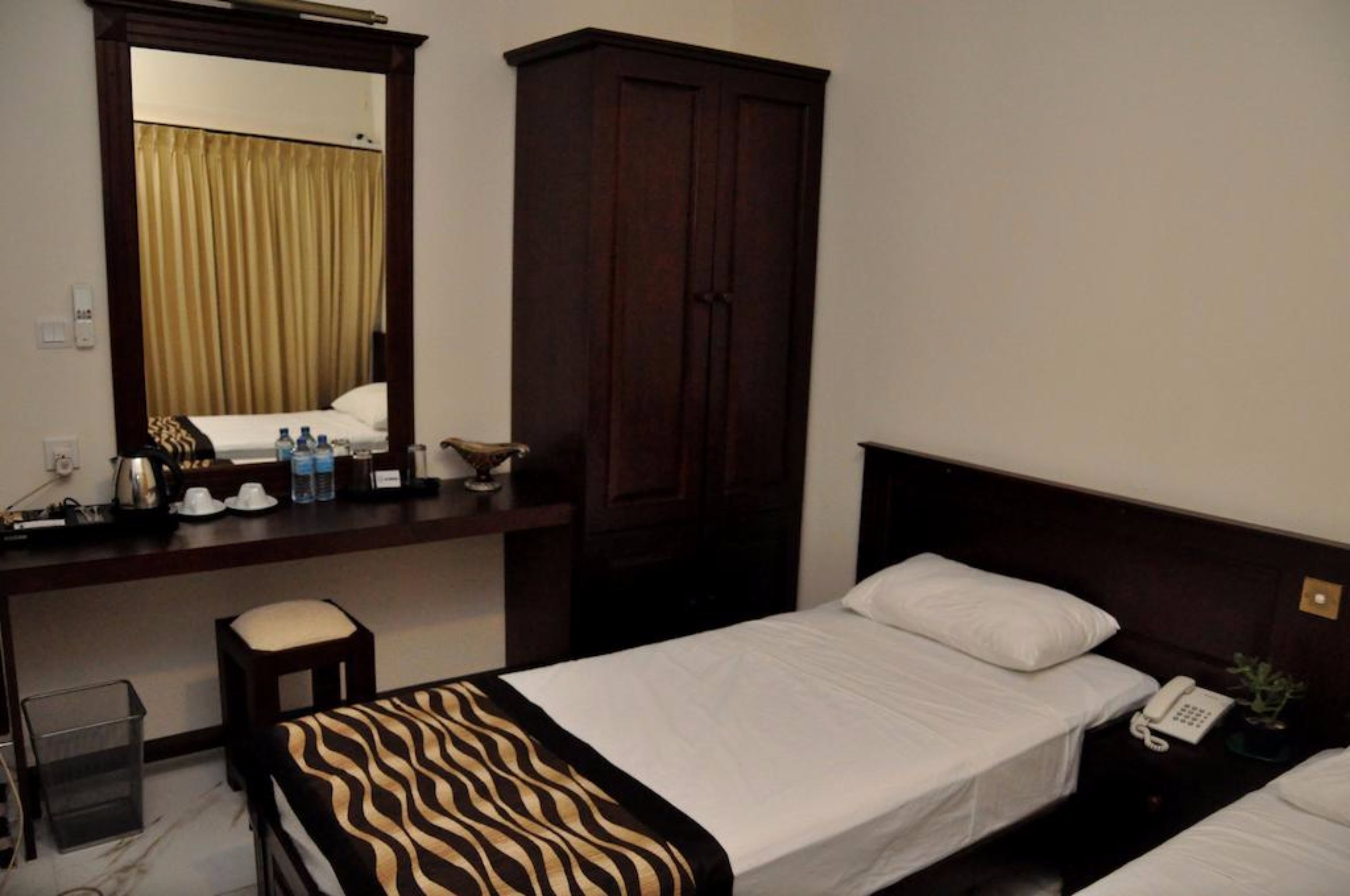 A hotel room with a bed, a desk, a chair, a wardrobe, and a mirror.