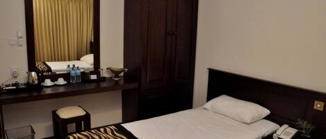 A hotel room with a bed, a desk, a chair, a wardrobe, and a mirror.