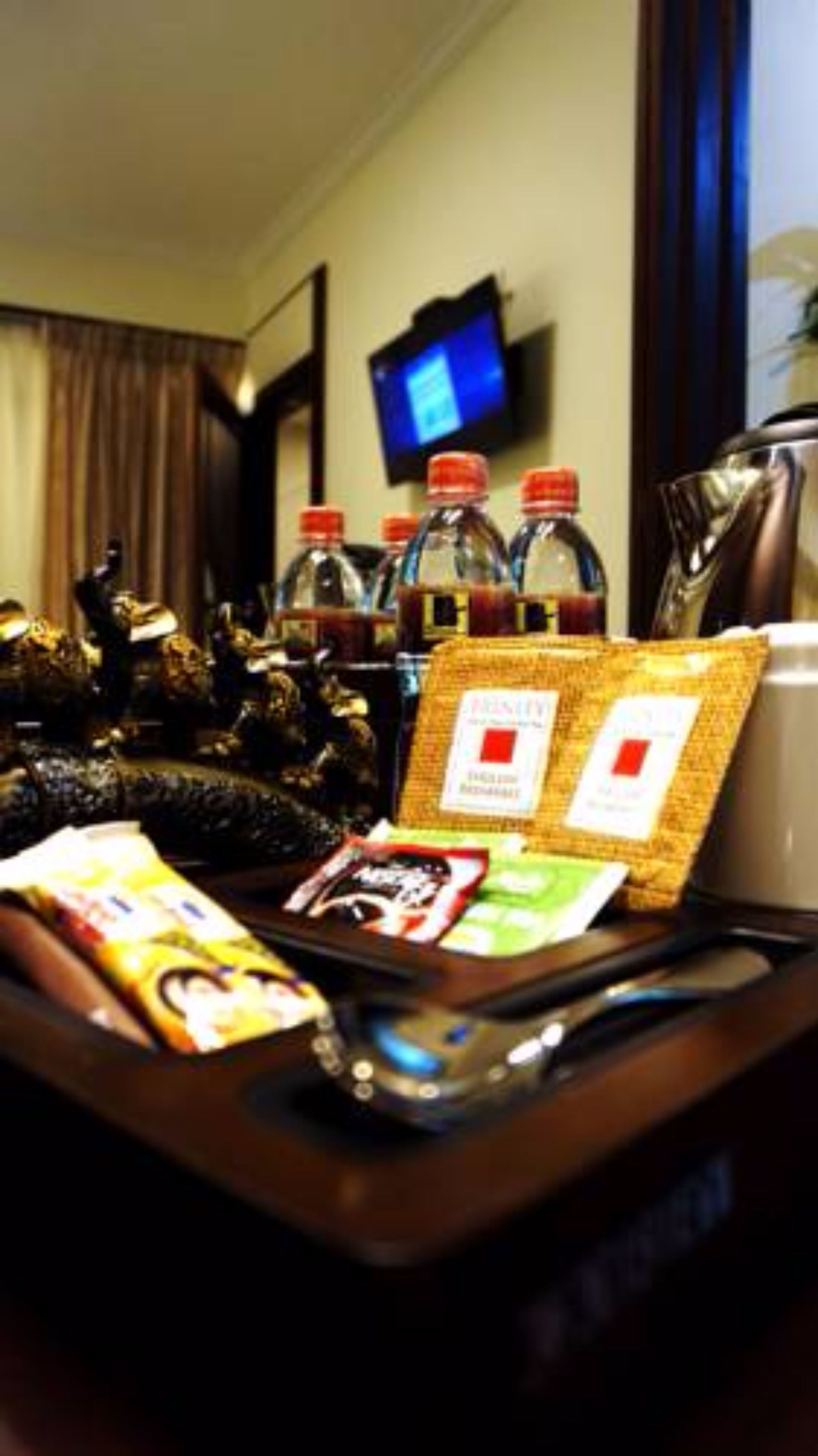 A hotel room with a desk, a television, and various items including snacks and a bottle of water.