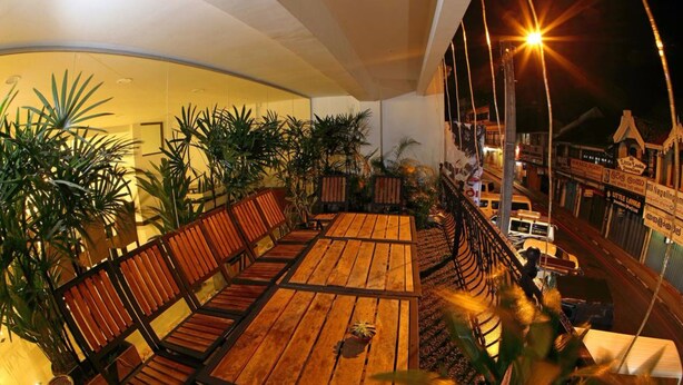 An outdoor seating area with wooden tables and chairs, surrounded by potted plants.