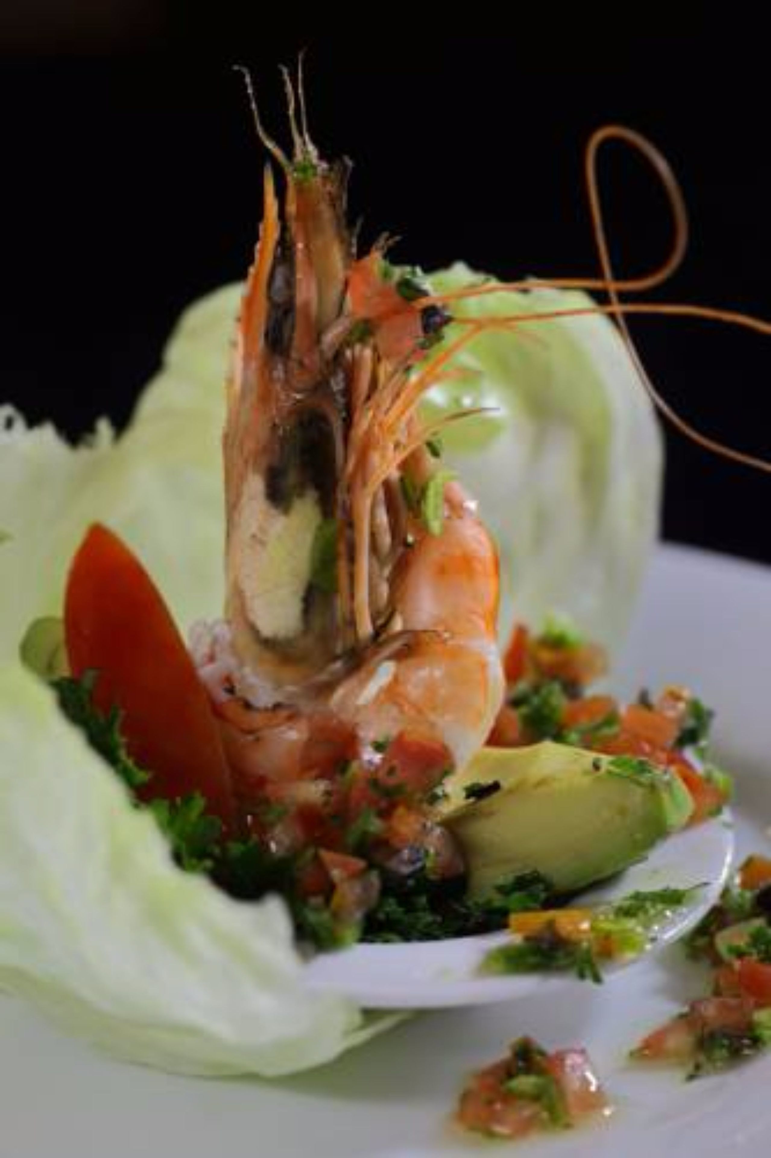 A shrimp dish with avocado and a salad on a white plate.