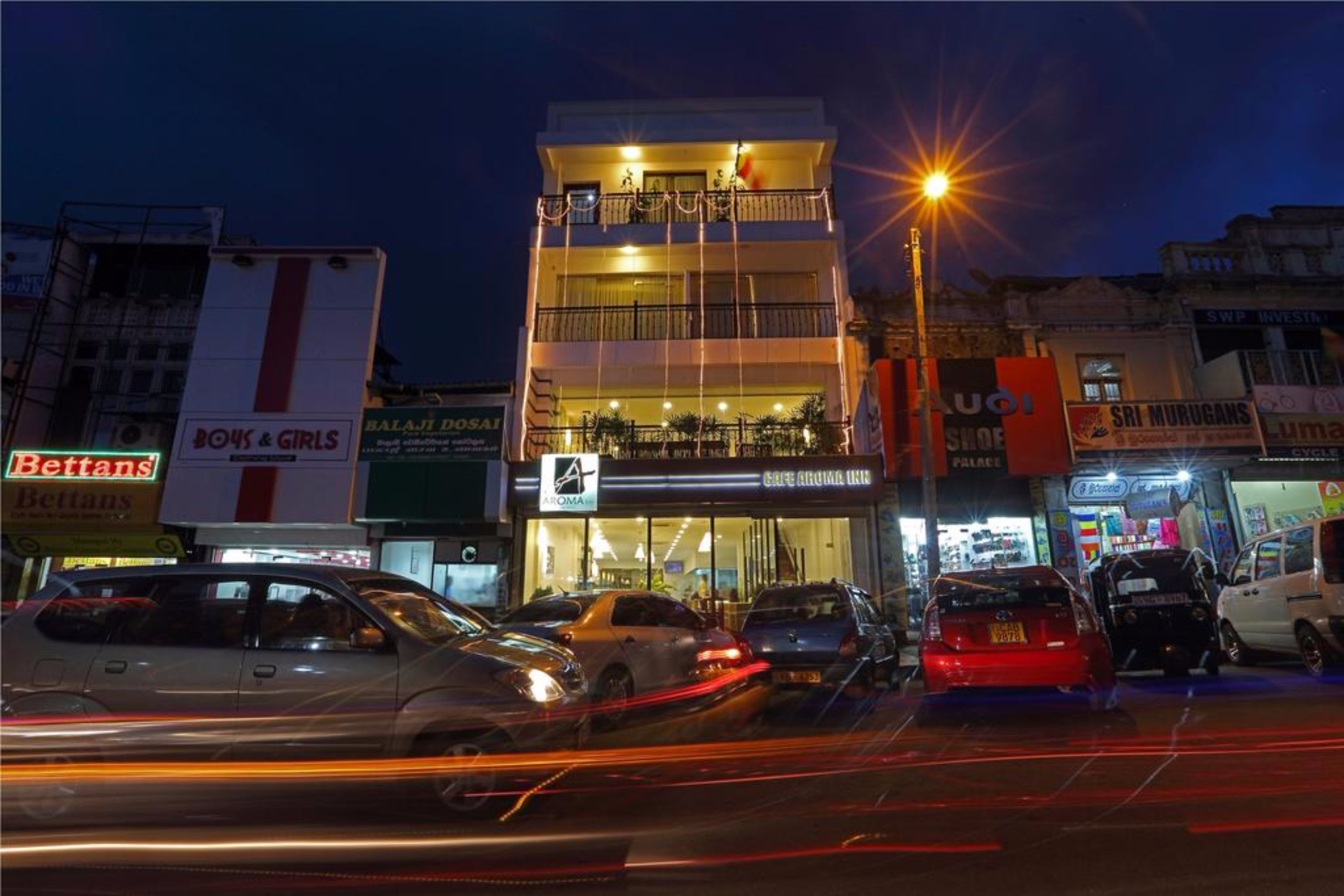 Un edificio de varios pisos con balcones, un restaurante visible y diversas tiendas en la planta baja.