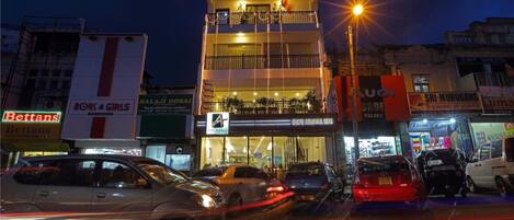 Un edificio de varios pisos con balcones, un restaurante visible y diversas tiendas en la planta baja.