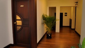 A hallway with a wooden door labeled 202, a potted plant, and a light fixture on the ceiling.