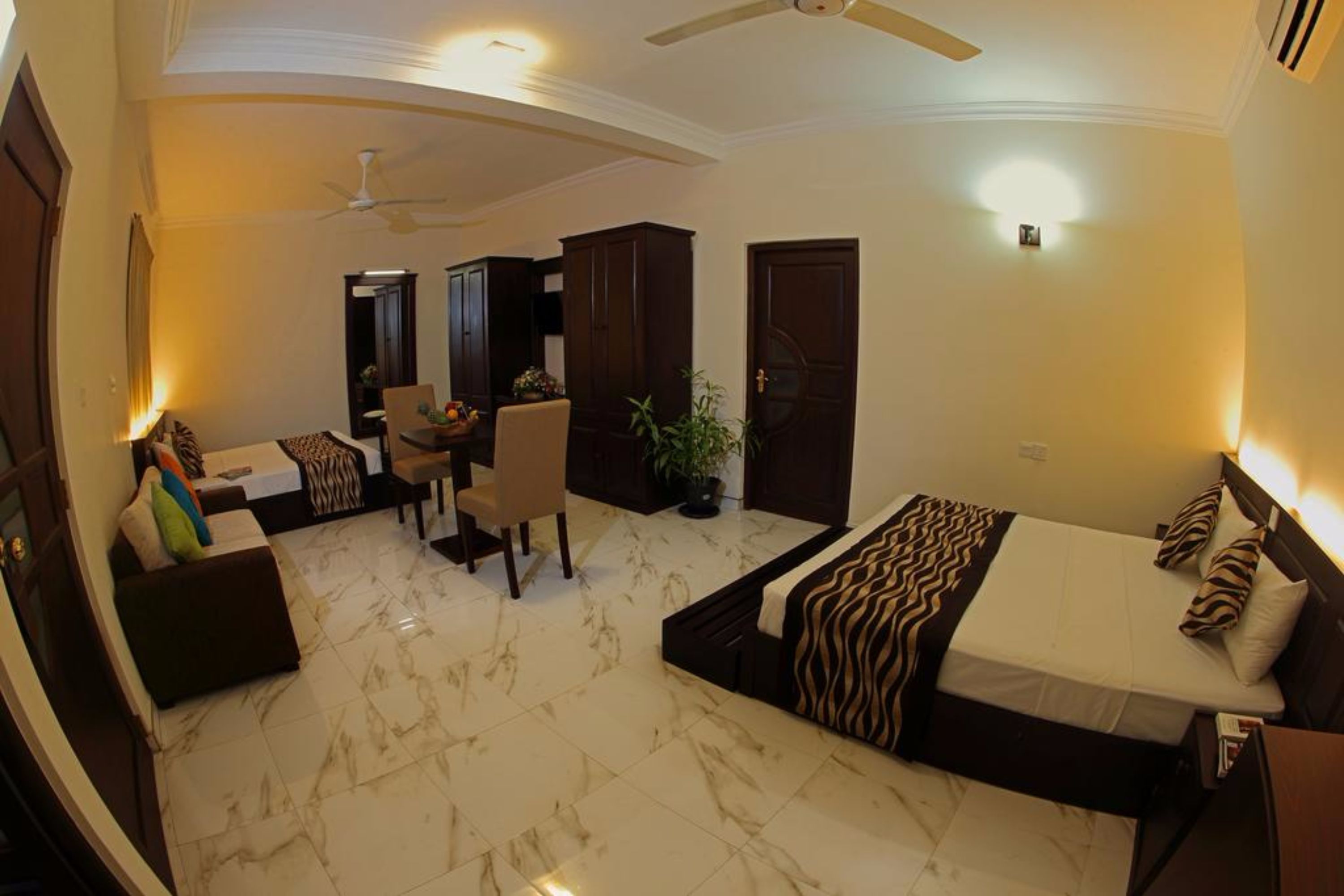 A hotel room with a bed, a sofa, a dining area, and a ceiling fan.